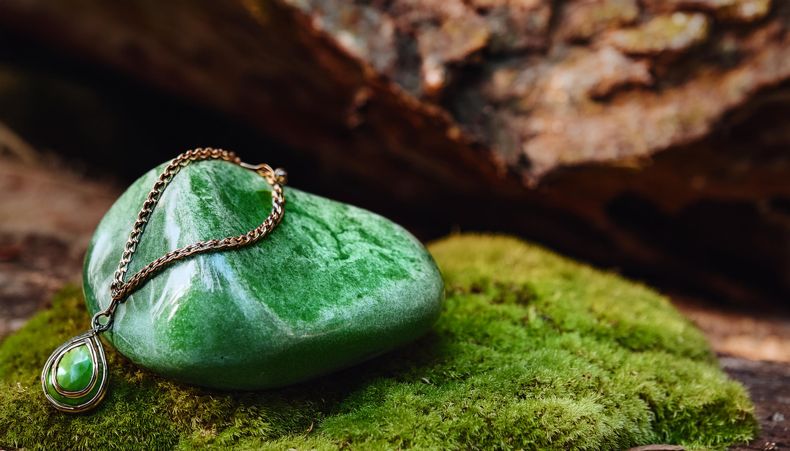 Jewlery with a green stone lying in a mossy wood.